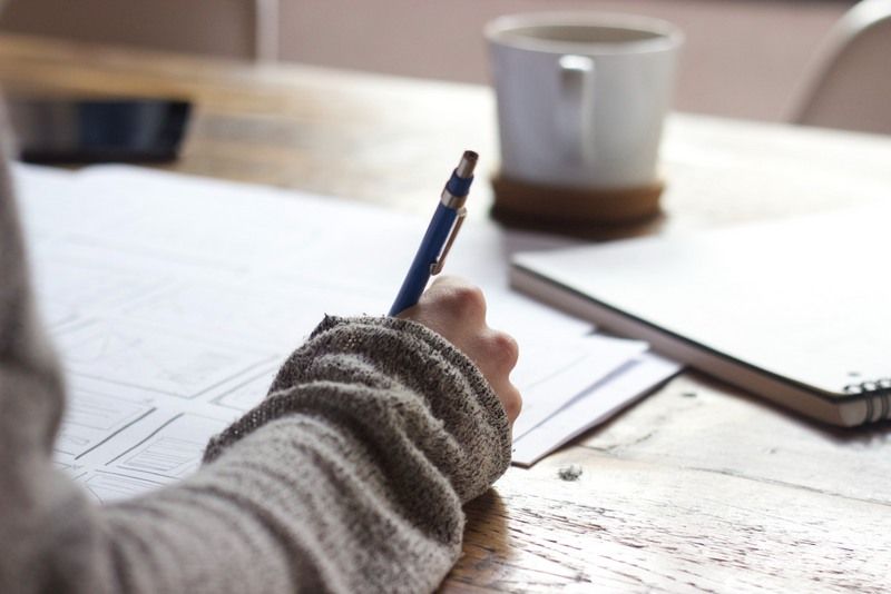 A Human Being Holding A Pencil And Writing Something.